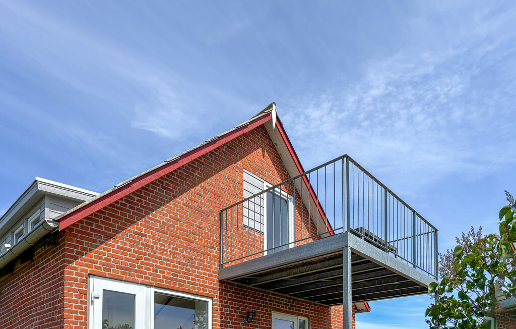 Een vakantiehuis met een lichte woonkamer en eetgedeelte in open indeling, waar grote ramen uitkijken op het platteland en uitkomen op een balkon. De gezamenlijke leefruimte zorgt ervoor dat iedereen ..