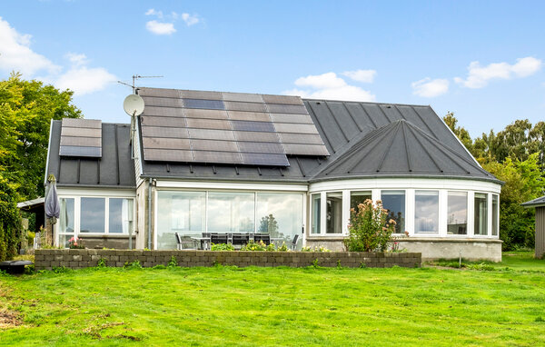 Natürliches Licht prägt den einladenden Wohnbereich, in dem eine geschwungene Fensterfront den Raum zur umliegenden Landschaft und zu Ausblicken auf das dahinterliegende Wasser öffnet. Großzügige..